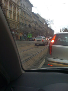 Az alábbi rendőrautó, a Ferenc kőrúton, abszolút tiszta forgalmi helyzetben, megkülönböztető jelzések nélkül halad a villamossínen.a pirosnál megállt..